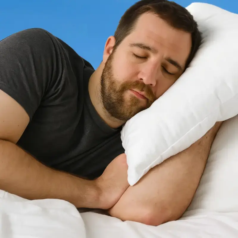 Mann liegt seitlich auf einem Kissen im Bett und ruht mit geschlossenen Augen.